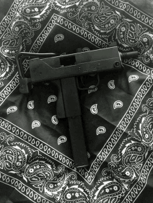 a gun is laying on a black bandana with white paisley patterns