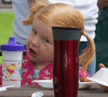 a little girl sitting at a picnic table with a red cup in front of her