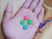 a hand holding four different colored gems in front of a wrapper