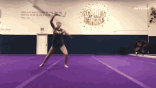 a cheerleader performs a trick on a purple mat in front of a wall that says golden all stars elite