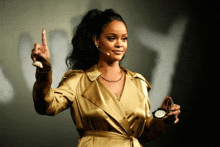 a woman in a gold trench coat is holding a powder and giving a speech