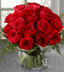 a glass vase filled with red roses and greenery