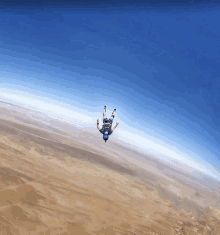 a man in a blue shirt is falling through the air over a desert