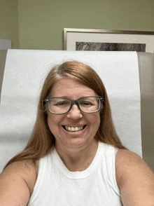 a woman wearing glasses is smiling while sitting in a hospital bed