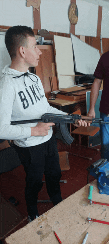 a boy wearing a white bike sweatshirt holds a gun