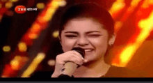 a woman singing into a microphone with a zee logo on the bottom right