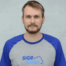 a man wearing a sige cloud shirt stands in front of a white wall