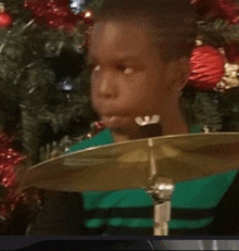 a young boy in a green shirt is playing drums in front of a christmas tree