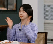 a woman in a plaid shirt is sitting at a table with a plate of food in front of her