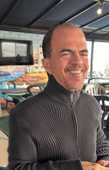 a man wearing a grey sweater is smiling in front of a brick wall