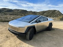 a silver tesla cybertruck is parked on a dirt road in the desert .