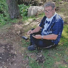 a man is sitting on the ground in the grass looking at his phone .