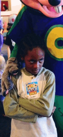 a little girl is standing in front of a chuck e cheese mascot holding a stuffed animal .