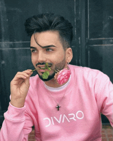 a man with a beard wearing a pink sweater is holding a rose in his mouth .