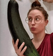 a woman wearing glasses is holding a very long cucumber .