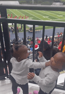 two little girls are standing next to each other in front of a football field with the letter t on it