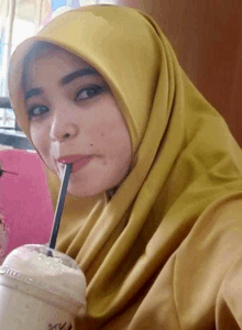 a woman wearing a yellow hijab is drinking through a straw .