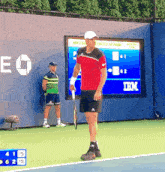 a man in a red shirt is holding a tennis racquet on a tennis court in front of an ibm sign