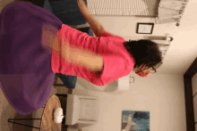 a woman in a pink shirt is spinning a purple skirt in a living room