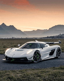 a white sports car is parked in a grassy field with mountains in the background