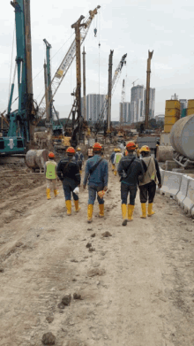 a group of construction workers are walking down a dirt road in front of a kobelco crane