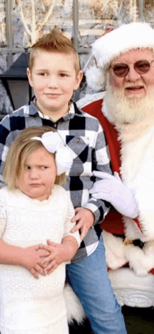 a boy and a girl pose for a picture with santa claus