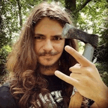 a man with long hair and a beard is holding a large axe and making a rock and roll sign .