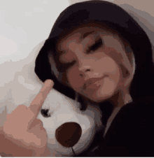 a woman is holding a teddy bear and giving the middle finger .