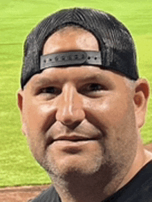 a man wearing a black hat and a black shirt is standing in front of a baseball field .