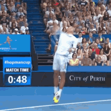 a tennis player is jumping in the air during a match with a city of perth sign in the background