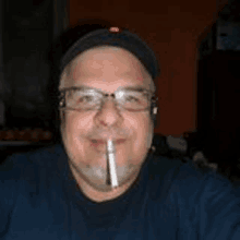 a man wearing glasses and a hat is smoking a cigarette in his mouth .