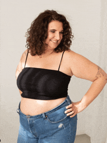 a woman wearing a black crop top and blue jeans is smiling