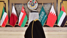 a man stands in front of a row of flags including one that says ' saudi arabia '