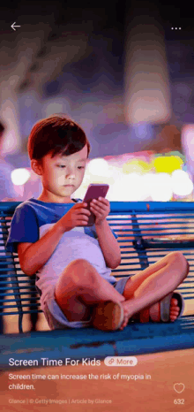 a little boy sits on a bench looking at his phone