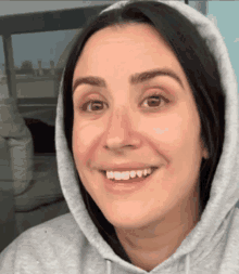 a woman wearing a grey hoodie with a hood is smiling