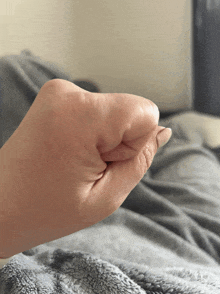 a close up of a person 's fist with a gray blanket in the background