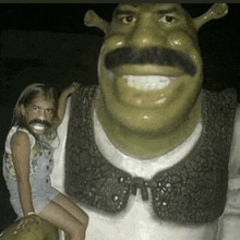 a girl is sitting next to a shrek statue with a fake mustache .