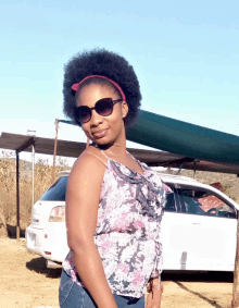 a woman wearing sunglasses and a headband stands in front of a car