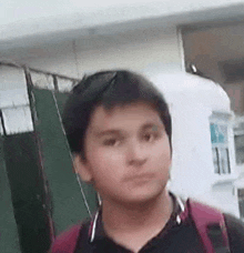 a young boy with a backpack is standing in front of a building and making a funny face .