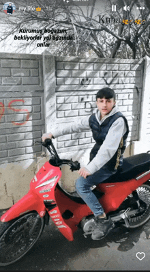 a young man is riding a red motorcycle in front of a white brick wall