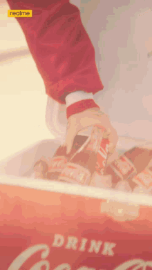 a person holding a bottle of coca cola in a cooler that says drink