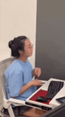 a woman in a blue shirt is sitting at a desk using a laptop computer .