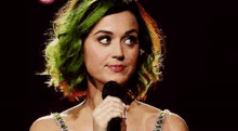 a woman with green hair is holding a microphone and making a funny face .