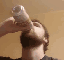 a man with a beard is drinking a can of beer from his mouth .