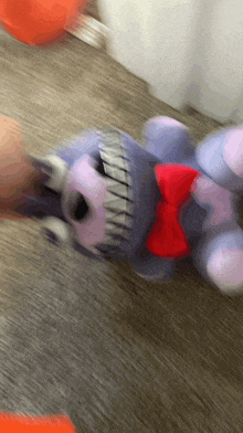 a purple stuffed animal with a red bow on its neck