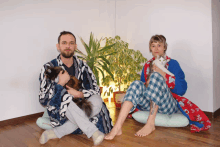 a man and a woman are sitting on the floor holding their cats