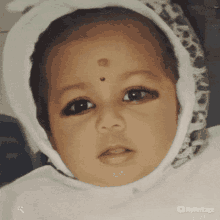 a baby wearing a white hood and a white bib with myheritage written on the bottom right corner