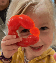 a little girl holding a red pepper in front of her eyes