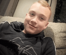 a young man is laying on a couch wearing a black shirt with the letter h on the front