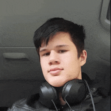 a young man wearing headphones and a leather jacket looks at the camera